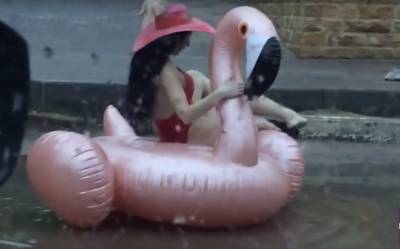 Девушка в купальнике плавает по лужам на розовом фламинго